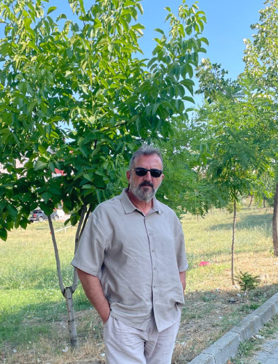Levent Uzakgören sahada, bir ağacın önünde